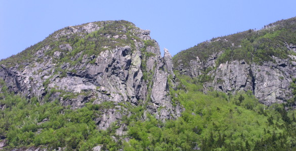 [Two photos stitched together showing craggy grey mountainous outcroppings with lots of greenery growing at lower levels.]